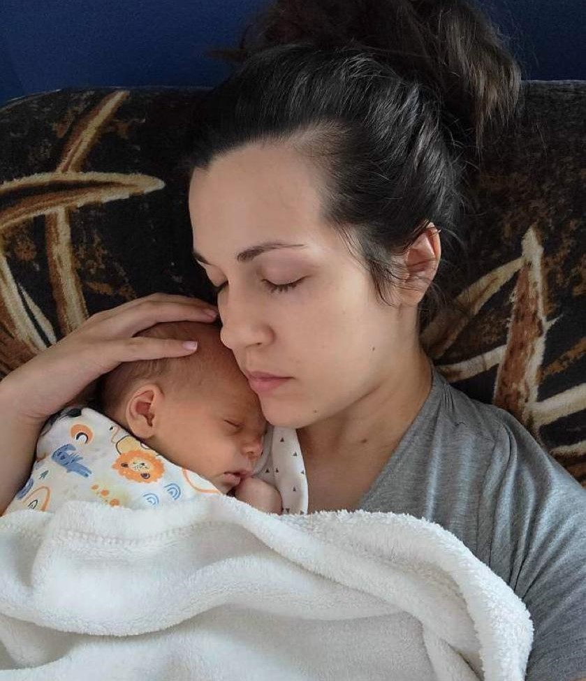 woman with dark hair has her eyes closed and is holding a baby wrapped in a blanket