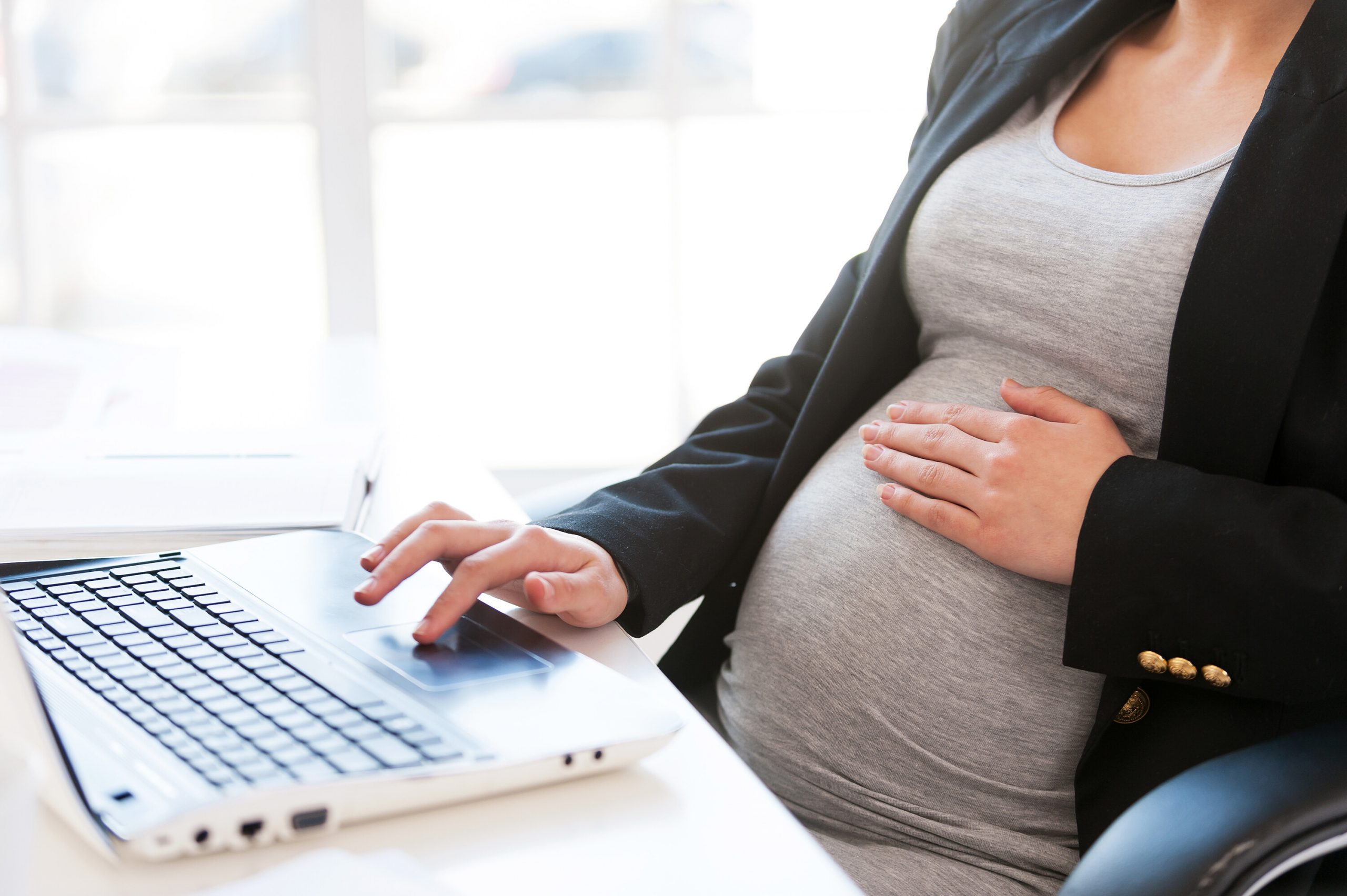 pregnant person with hand on their belly while using a laptop computer