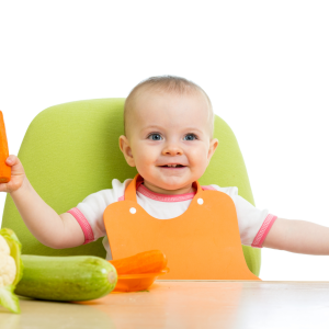 baby sitting at a green highchair eating vegetables